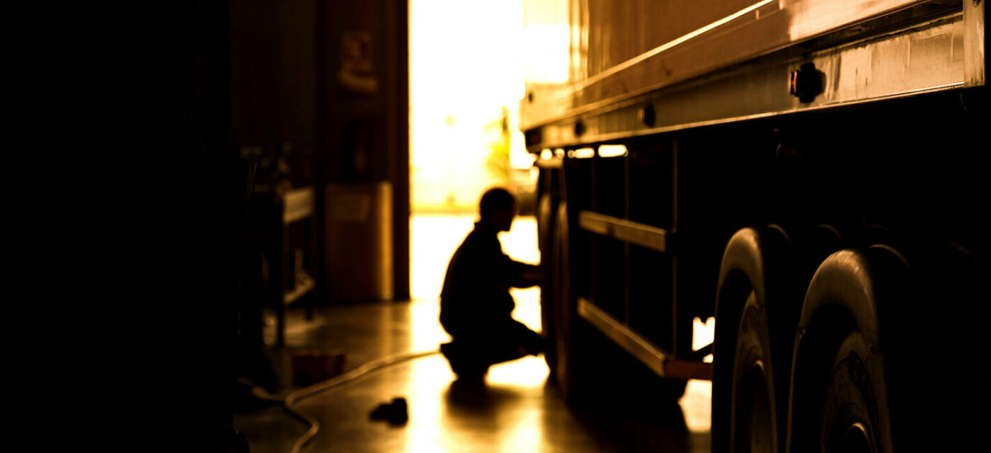 A kneeling person by a truck tire silhouetted against an open door