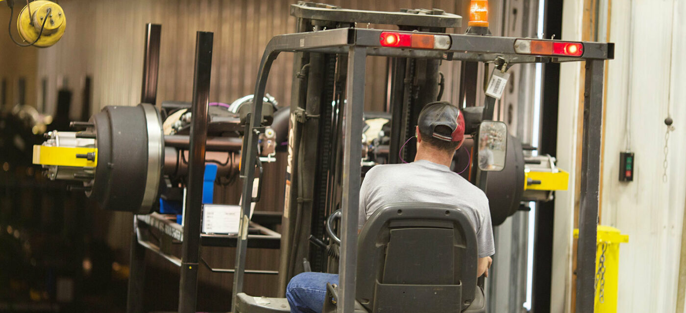 A man operating a forklift to load a lift axle on a semi truck trailer
