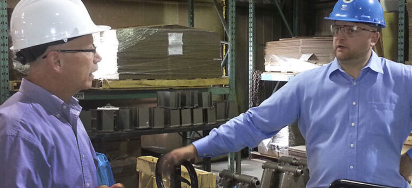 Two men in a warehouse wearing hardhats talking