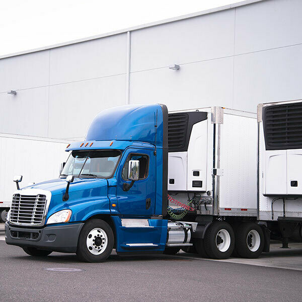 A blue semi cab hooking up to a trailer