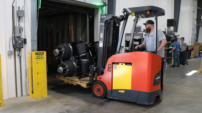 Man using forklift to load an auxiliary suspension into a trailer