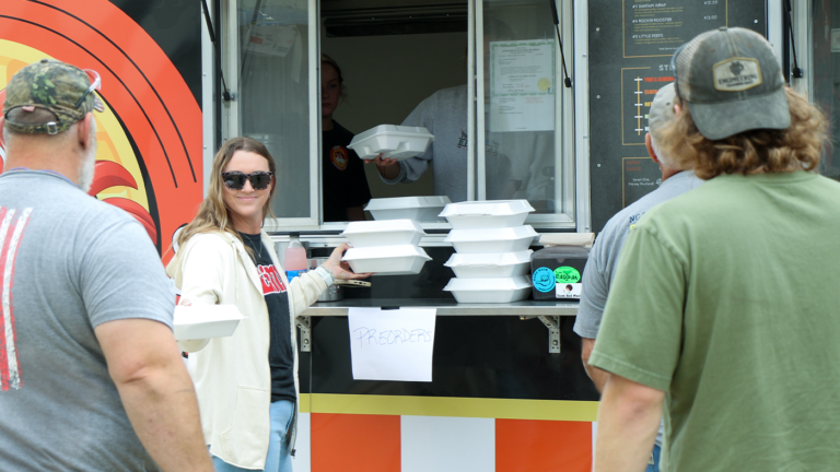 Woman holding out takeout container from food truck to approaching man