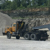 Work trucks in a quarry, one with a dump trailer.