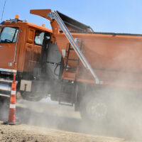 An orange dump truck with a lift axle driving up a dirt incline