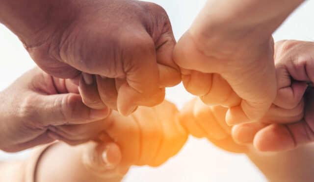 6 people holding fists together in a circle