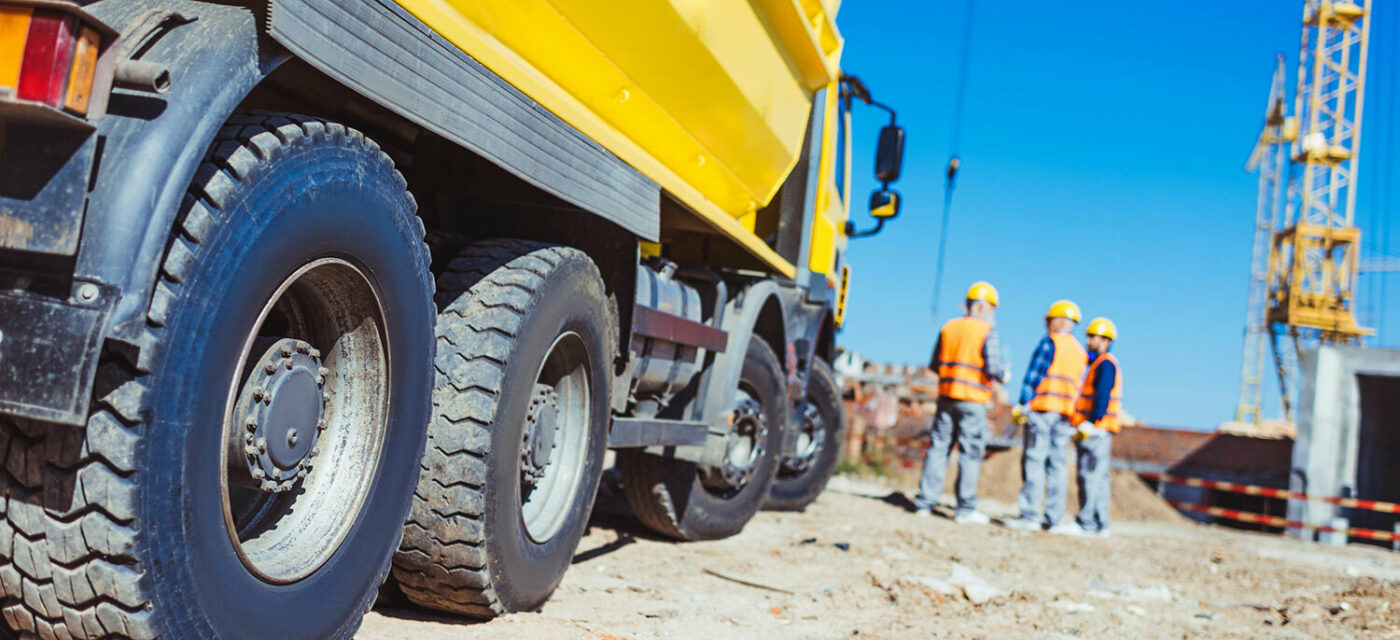 A low side angle photo of a yellow dump truck with three construction men to its right