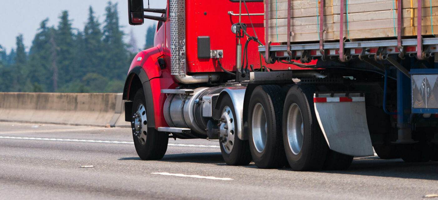 A red semi truck on a highway hauling a flatbed trailer with wood