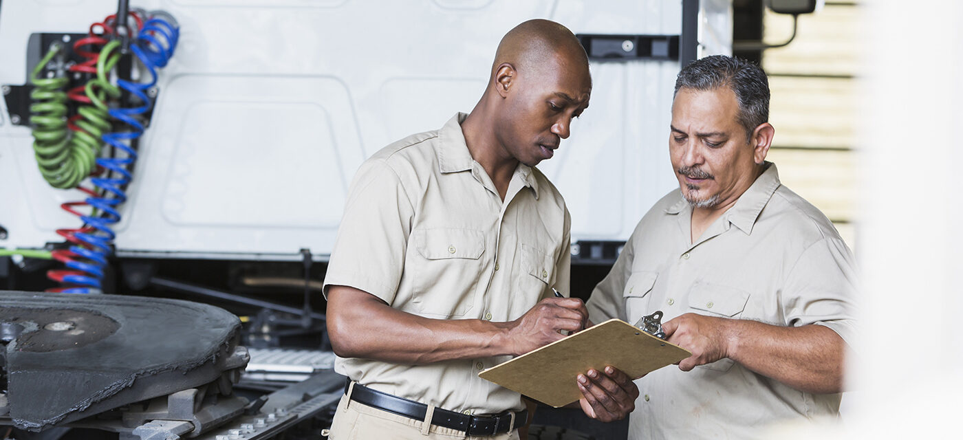 Two men looking at a clipboard behind a white semi truck