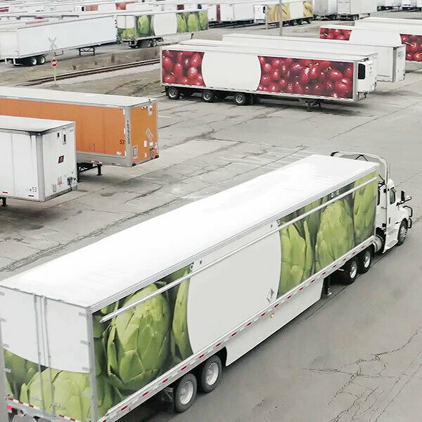 A semi truck with an enclosed trailer driving past several parked trailers