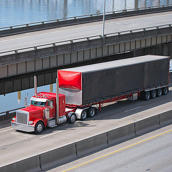 A red semi truck hauling a trailer over a bridge