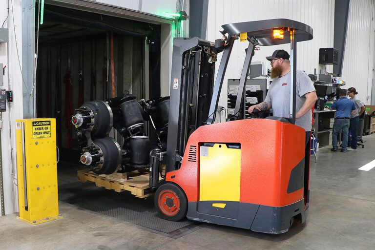 Man loading lift axles in trailer with forklift