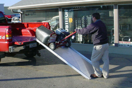 A man using a link portable ramp to unload equipment from the back of a pickup truck