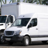 A white box truck behind a white cargo van