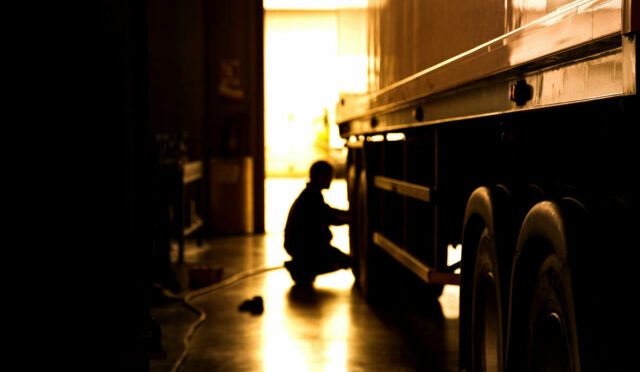 A kneeling person by a truck tire silhouetted against an open door
