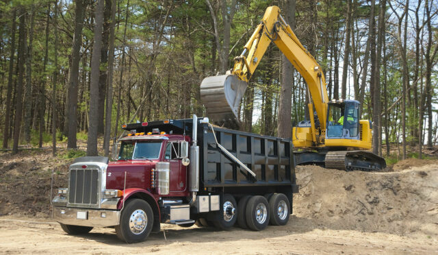 A dump truck equipped with a Link Auxiliary Suspension being loaded with dirt