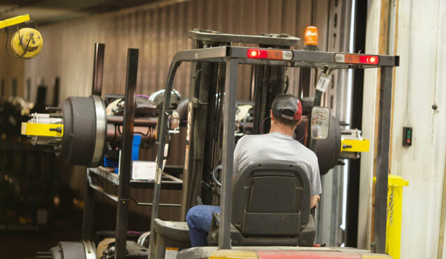 A man operating a forklift to load a lift axle on a semi truck trailer