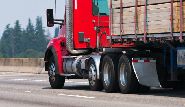 A red semi truck on a highway hauling a flatbed trailer with wood