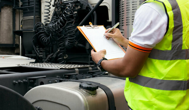 A man in a safety jacket marking a checklist by the rear of a semi truck cabin