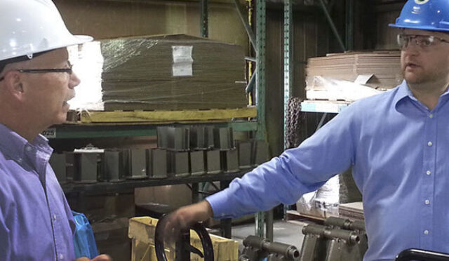 Two men in a warehouse wearing hardhats talking