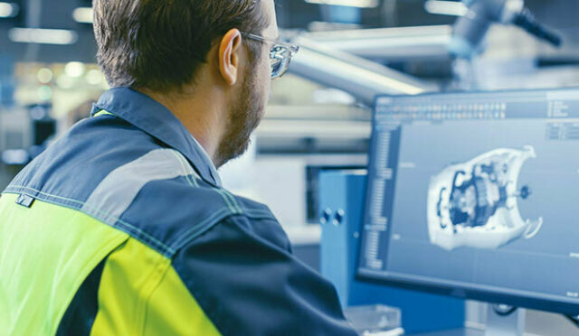 A photo over a man's shoulder as he looks at a part rendering on a computer screen