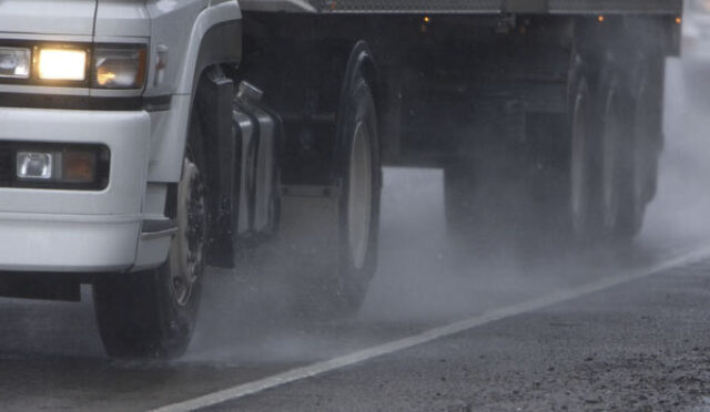 A photo of a semi truck's tires on a road in the rain